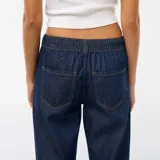Pantalón de jean con corte baggy y pierna ancha, de tiro medio y color azul oscuro, con cierre frontal y bolsillos laterales.