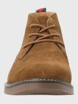 Bota tipo chukka de Hush Puppies, confeccionada en descarne color marrón, con cordones al tono, suela de goma y detalle de tirador en el talón con franjas rojas y negras.