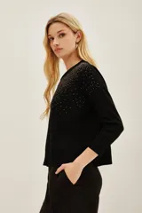 Sweater negro de manga larga con cuello redondo, decorado con apliques brillantes que simulan un degradé o salpicado en la parte superior del pecho y hombros.