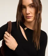 Blusa negra de punto acanalado, con mangas largas, cuello redondo con detalle metálico dorado y abertura asimétrica en el hombro.