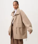 Campera cortaviento oversized color beige, de cuello alto, mangas largas con puños elásticos, bolsillos frontales con solapa y cordón ajustable en la cintura.