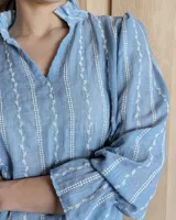 Blusa de algodón con cuello mao y volados, mangas largas con puños elásticos y corte holgado.