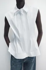 Camisa de cuello solapa y manga sisa, de color blanco. Presenta bajo acabado en peplum y cierre frontal con botones ocultos.