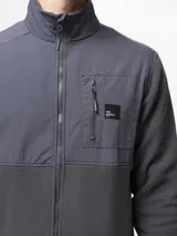 Campera de polar negro con paneles de nylon en el pecho, cuello alto, cierre frontal completo, bolsillo con cierre en el pecho y bolsillos laterales con cierre.