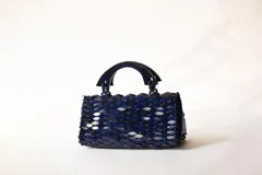 Cartera de mano azul de diseño estructurado, confeccionada con piezas texturizadas entrelazadas y manijas rígidas de madera.