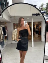 Pollera corta de cuero sintético con diseño de paneles y bolsillos frontales grandes. Presenta un corte recto y tiro medio.