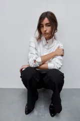 Camisa blanca de calce relajado con acabado satinado y brillo sutil, cuello clásico, cierre frontal con botones y mangas largas con puños.