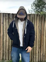 Campera de pana negra con capucha incorporada, bolsillos laterales y cierre frontal con botones a presión y cremallera.