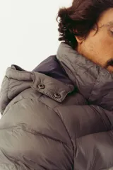Campera puffer de abrigo con diseño bicolor, gris en la parte superior y violeta oscuro en la inferior. Cuenta con cierre frontal completo, capucha desmontable, bolsillos laterales con cierre y logo estampado en el pecho.