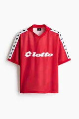 Camiseta de futbol de manga corta de la marca Lotto, en color rojo con un sutil estampado geométrico. Cuenta con cuello tipo polo abierto con escote en V y un calce holgado. Las mangas presentan una franja blanca lateral decorada con el logo de la marca repetido. El logotipo de Lotto destaca en blanco en el centro del pecho.
