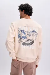 Buzo de felpa oversize color crudo, con cuello redondo y diseño gráfico estampado en la espalda que muestra un paisaje montañoso y un auto con el texto "WILD WEST ADVENTURE".