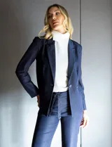 Blazer de tencel color azul marino con cuello de solapa y cierre frontal de un solo botón. Presenta bolsillos delanteros simulados con detalle de vivo trenzado y un diseño estructurado de calce entallado.
