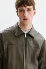 Cazadora estilo bomber en tejido revestido color verde militar, con cuello clásico, cierre frontal de cremallera metálica, bolsillos laterales y elástico fruncido en el bajo y los puños.