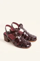 Sandalia plateada de cuero con tiras entrecruzadas, taco de madera y hebilla lateral.