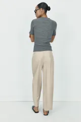 Pantalón de tiro alto con corte recto, bolsillos delanteros y detalle de pinzas con botones en la cintura. Cuenta con cierre frontal de cremallera y gancho metálico.