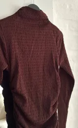 Vestido corto de manga larga en color bordó, con cuello alto y diseño ajustado con frunces laterales que recorren toda la prenda.