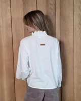 Camisa de manga larga con estampado de cuadros en tonos azules y rojizos. Presenta un cuello alto con volados y puños elásticos con detalle de volado en el extremo. Cierre frontal con botones ocultos.