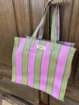 Bolso tipo tote bag con estampado a rayas verticales en tonos verde, rosa, celeste y marrón. Tiene asas de hombro y un parche con la inscripción "AMÉN".