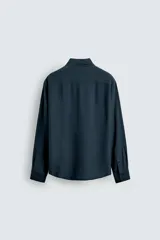 Camisa de corte relajado confeccionada en tejido fluido con mezcla de viscosa. Presenta cuello italiano, manga larga con puños abotonados y cierre frontal con botonadura, destacando por el detalle de jaretas verticales a ambos lados de la tapeta.