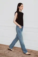 Jeans de tiro medio con corte recto y largo completo. Presentan un diseño de cinco bolsillos, cierre frontal con cremallera y botón, y un acabado con efecto lavado. Incluyen detalles de roturas y parches decorativos en la parte delantera.