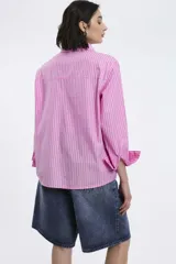 Camisa oversize de popelina a rayas celestes y blancas, con cuello camisero, manga larga con puños abotonados, cierre frontal con botones y un bolsillo en el pecho con etiqueta bordada.