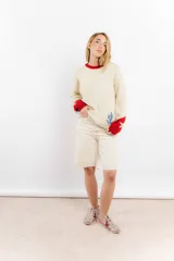 Sweater tejido a mano en lana merino color crudo, con cuello y puños en rojo. Presenta un diseño con motivos de un cowboy y estrellas.