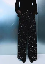 Jeans rectos de tiro medio en tejido de algodón vaquero color negro, con diseño de cinco bolsillos, trabillas para cinturón y cierre frontal con botón y cremallera. Presenta aplicaciones de tachuelas brillantes a lo largo de las piernas.
