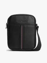 Morral de cuero sintético con acabado granulado color negro, de Tommy Hilfiger. Cuenta con un compartimento principal con cierre de cremallera, bolsillo frontal decorado con una franja tricolor vertical, correa cruzada ajustable y el logo metálico de la marca en la parte superior.