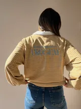 Buzo tipo chomba de corte oversize con diseño a rayas horizontales celestes y blancas. Presenta cuello camisero blanco y un bordado en la espalda con la inscripción República Oriental del Uruguay.