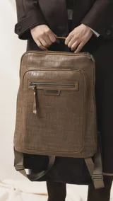 Mochila de diseño rectangular con textura símil cuero efecto cocodrilo en color tostado. Cuenta con un bolsillo frontal con cierre, compartimento principal con doble cierre, correas ajustables y manija superior. Incluye detalles metálicos y placa con logo de la marca.