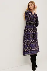 Vestido midi de viscosa con estampado estilo ikat en tonos oscuros, violetas y azules. Presenta mangas largas, cuello redondo y un diseño holgado que se ajusta a la cintura mediante un cinturón.
