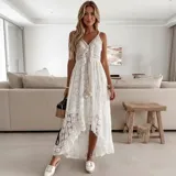 Vestido largo de encaje calado color blanco, con diseño de falda irregular más corta adelante. Presenta escote en V con cordones decorativos y borlas, tirantes finos y detalle de cintura marcada.