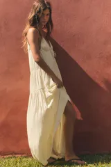 Vestido largo color crudo de tela satinada, con escote en V, tirantes finos ajustables, detalle de cordón ajustable en el pecho y diseño fruncido en capas.
