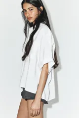 Camisa de corte fluido confeccionada en mezcla de modal, con cuello solapa, manga corta y bolsillo de plastrón en el delantero. Presenta cierre frontal con botones ocultos por tapeta y bajo con aberturas laterales.