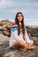 Sweater tejido a mano en lana merino color crudo, con cuello redondo y diseño de rayas horizontales en tonos rojo, amarillo, azul y verde en la parte superior.