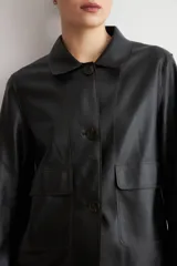 Chaqueta de eco cuero negro con cuello camisero, cierre frontal oculto y mangas largas con puños rectos.