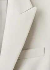 Blazer sastre entallado color beige, con cuello en pico, solapas de muesca, manga larga y bolsillos con solapa en la parte delantera.