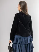 Chaqueta de terciopelo negro con bordados florales y ornamentales en tonos dorados, rosados y azules. Presenta un corte recto, cuello redondo y cierre frontal abierto con detalles de costuras decorativas en los bordes.