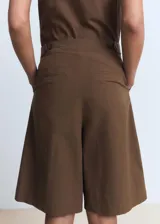 Short marrón de corte recto y largo bermuda, con diseño de pinzas en la parte delantera, bolsillos laterales y cierre frontal oculto.