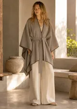 Ruana de corte amplio y diseño envolvente, color beige con bordes terminados en costura decorativa de hilo negro. Incluye un cinturón del mismo material para ajustar a la cintura.
