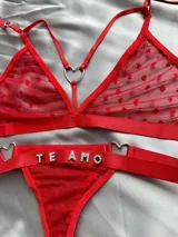 Conjunto de lencería rojo de tul con diseño de corazones aterciopelados en relieve. Incluye un soutien tipo triángulo con argollas metálicas en forma de corazón y tiras regulables, y una bombacha colaless con tiras laterales ajustables unidas por argollas en forma de corazón y el texto "TE AMO" aplicado con apliques de pedrería brillante.