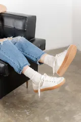 Zapatillas color marfil con detalles dorados en el talón y ojales metálicos. Suela de goma caramelo y cordones beige.