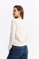 Remera de manga larga color verde oliva, con cuello redondo y estampa gráfica pequeña en el pecho con texto y dibujos lineales.