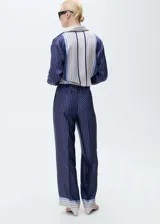 Pantalon de corte recto y diseño fluido con acabado satinado. Presenta un estampado de rayas verticales con detalles de franjas horizontales en el ruedo, cierre frontal con botón y cremallera, pinzas en la cintura y bolsillos laterales.