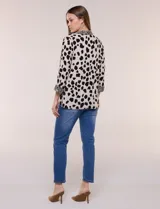 Camisa holgada de rayón con estampado animal print de manchas negras sobre fondo beige, cuello camisero y abotonadura frontal con detalles de estampa estilo cebra. Cuenta con mangas tres cuartos y ruedo curvo.
