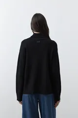 Polera de tejido liviano en color negro, con cuello alto, mangas largas y corte relajado. Presenta un diseño minimalista con recortes laterales que aportan estructura a la prenda.
