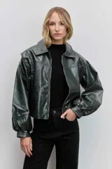 Cazadora de estilo bomber confeccionada en material efecto piel color verde oscuro. Presenta cuello camisero, cierre frontal con cremallera, mangas largas abullonadas con puños elásticos y un corte ligeramente cropped.