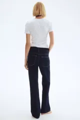 Jeans de cinco bolsillos en denim de algodón con leve stretch, color azul oscuro. Modelo de corte ajustado de cintura a muslo, más holgado de rodilla a bajo, con pierna acampanada (corte para bota) y tiro alto con cierre y botón.