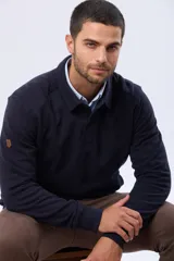 Buzo de felpa color verde oscuro, con cuello tipo polo, cierre frontal parcial con botones y bolsillos laterales. Presenta puños y ruedo acanalados.