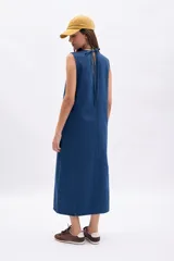 Vestido largo sin mangas de denim azul, con corte recto y holgado, costura central vertical y bolsillos laterales.